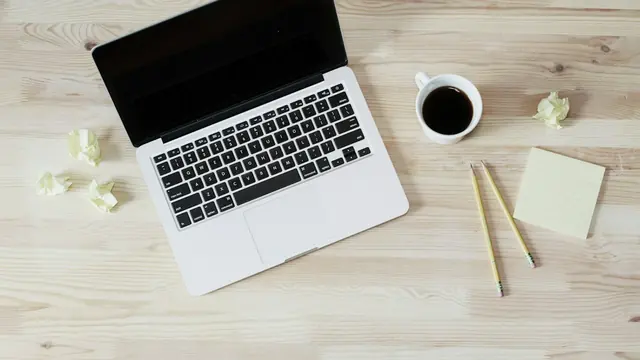 Portátil, taza de café y bolas de papel arrugado sobre una mesa