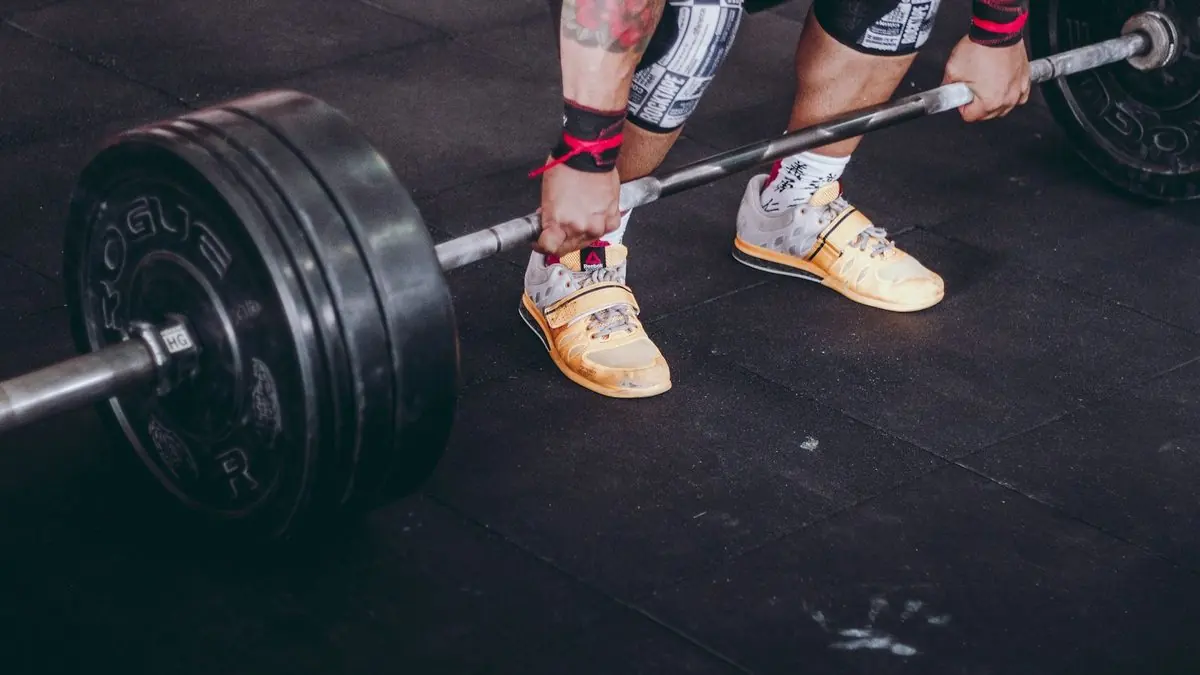 Barra con discos en el suelo de un gimnasio, con una persona a punto de levantarla