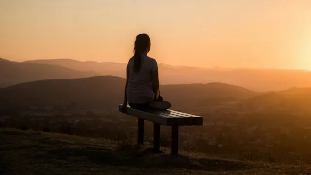Mujer sentada en un banco mirando las montañas al atardecer
