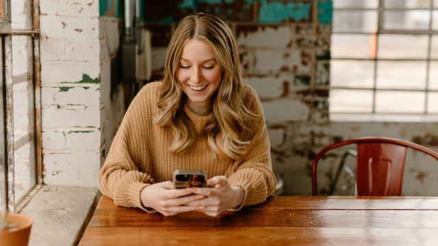 Chica sonriendo mientras mira el móvil en una mesa